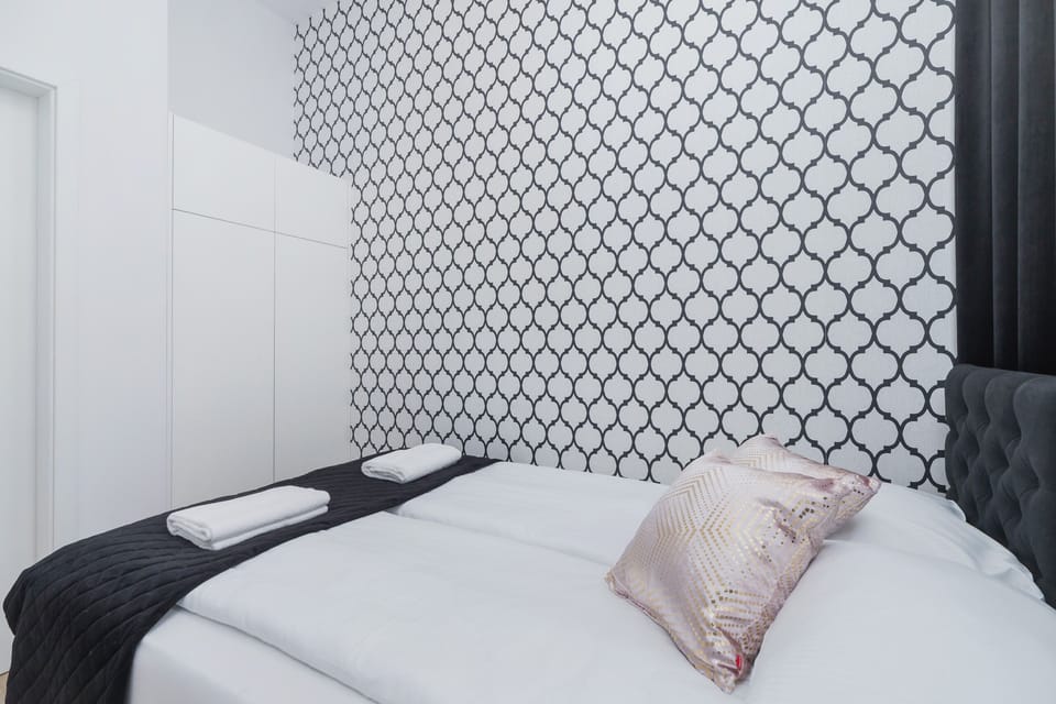 A bright bedroom featuring patterned wallpaper and a comfortable bed. Simple, elegant décor makes the space inviting.
