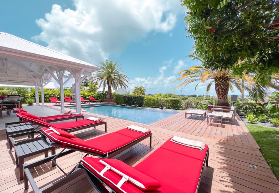 Discover our luxury villa in the West Indies with panoramic views of the infinity pool, surrounded by red deckchairs and a garden armchair. Immerse yourself in the tropical ambience of our magnificent lush garden. Enjoy an unforgettable stay where relaxation and elegance meet. Book now for a dream vacation in paradise.