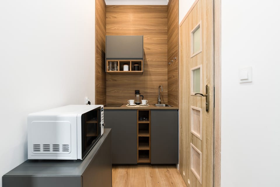 A compact kitchenette with wooden cabinetry, a microwave, and modern appliances, blending functionality with style.
