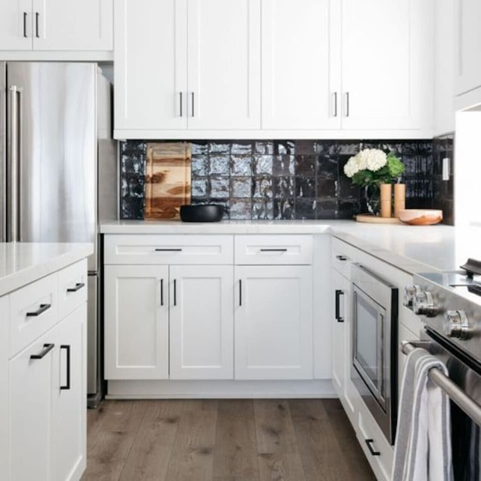 Modern kitchen w/ white cabinetry, dark backsplash & sleek finishes