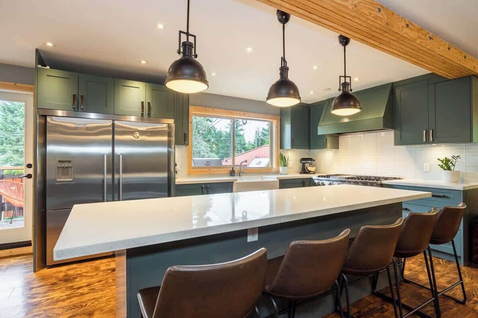 - Sleek kitchen featuring double fridge, wide island seating, and pendant lights  
- Perfect for group meals with stainless appliances and modern cabinetry  
- Enjoy cooking surrounded by warm wood tones and forest views outside  
