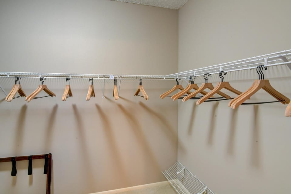 Walk-in closet with beige walls, white wire shelving, and wooden hangers along two walls.