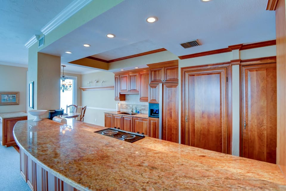 Granite countertop curves around a kitchen with cherry wood cabinets and built-in electric cooktop.