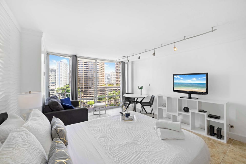 Bright studio with a queen bed, sofa, and a cute table