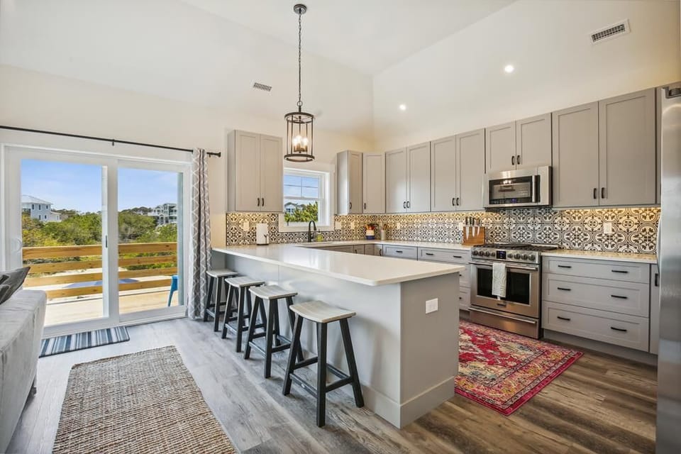 Your gourmet kitchen features a spacious island, high-end appliances, and stylish patterned backsplash—perfect for cooking and gathering with loved ones. Natural light pours in from the patio doors.