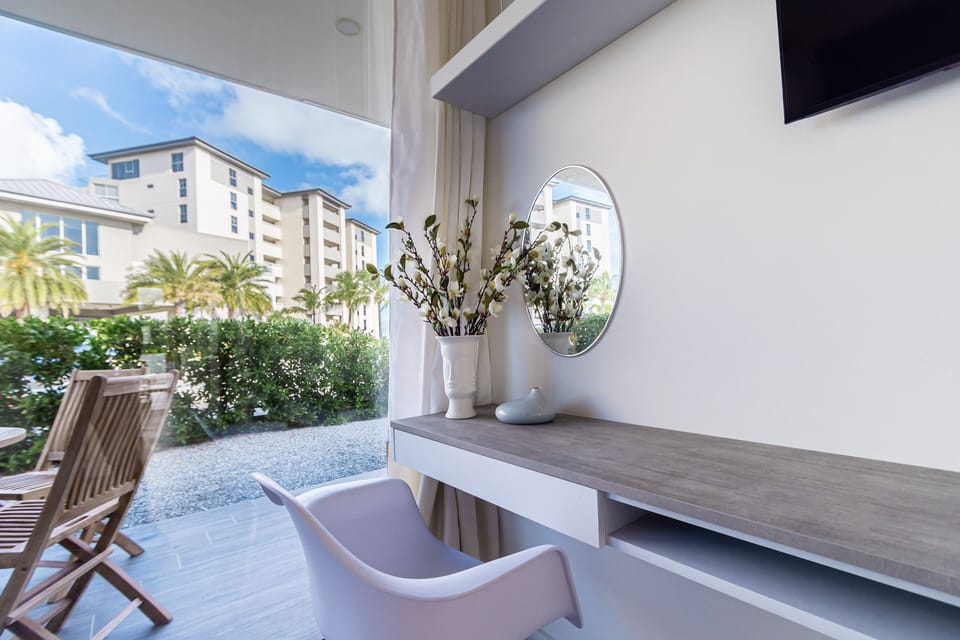 Relax in your bright, modern living space where expansive windows frame palm trees and tropical greenery, creating a serene indoor-outdoor retreat for your getaway.
