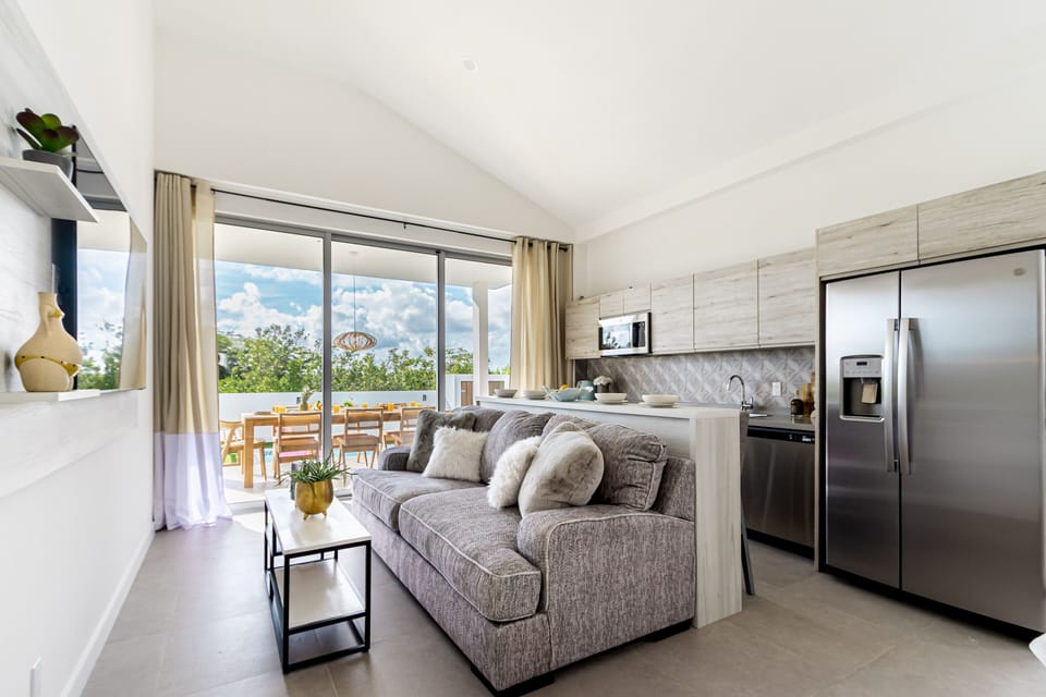 Your bright, open-concept retreat blends comfort and style with a plush sofa, modern kitchen, and stunning natural views through expansive windows.