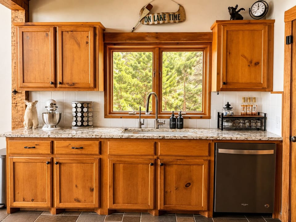 Fully equipped kitchen with warm wood cabinetry, granite countertops, stainless steel appliances, and peaceful wooded views from the kitchen window.