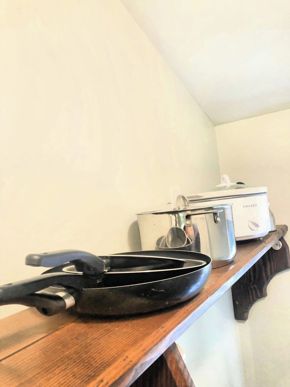 Fry panes, a pot, and a slow cooker on the upper shelf in a kitchenette