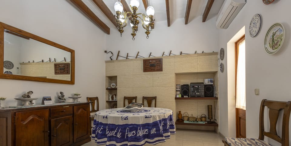 Inviting Mallorcan-style dining room with exposed wooden beams, solid wood furniture and a central round table, featuring traditional décor and a built-in shelving unit that adds warmth and character.