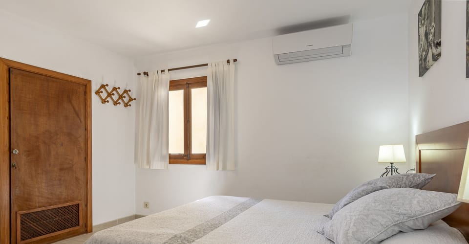 Bright bedroom with a double bed, neutral-toned textiles, air conditioning and warm wooden details, creating a calm and comfortable atmosphere for restful nights.