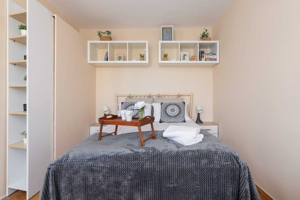 A cozy bed with decorative pillows and shelves for storage above it.

