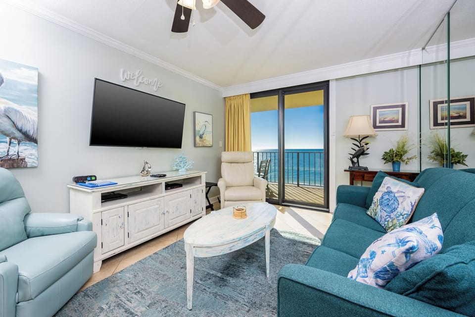 This living area features a large TV, cozy seating, queen sofa-sleeper, and a breathtaking view of the beach from the balcony