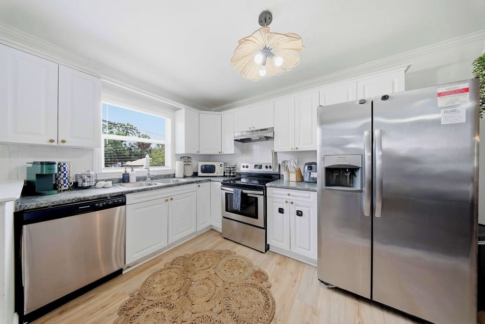 The heart of the home. This beautiful kitchen blends clean white cabinetry with a woven jute rug and a stunning rattan light fixture, creating an inviting space to cook and gather.