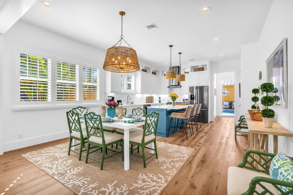 The dining area is unique with its bright green dining chairs, frosted glass-topped table, and seating for 8. Towering above is an eye-catching basket light fixture. The open plan dining area sits between the living room and kitchen.