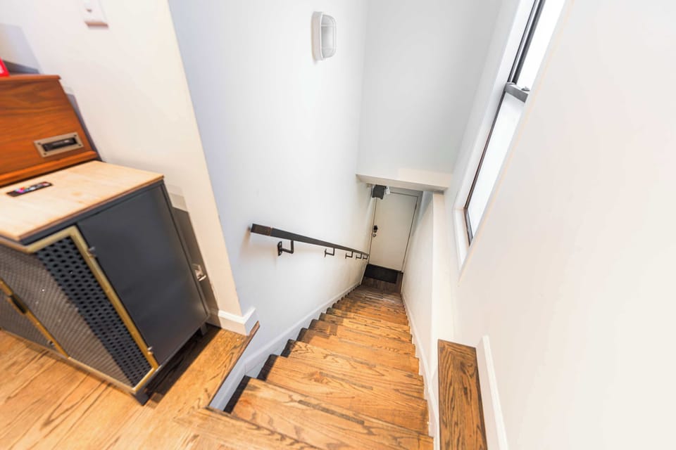 Step inside and head up the beautiful oak-tread staircase. This bright entryway features a minimalist black handrail, clean white walls, and a tall window that fills the space with natural light, leading you directly into the home's dining area.