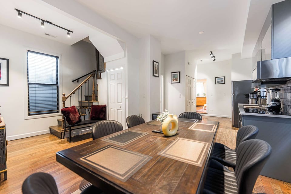 Enjoy meals in this stylish open-concept dining area featuring a rustic wood table and modern seating. Bathed in natural light from large windows, it flows seamlessly into a sleek kitchen with stainless steel appliances and dark cabinetry.