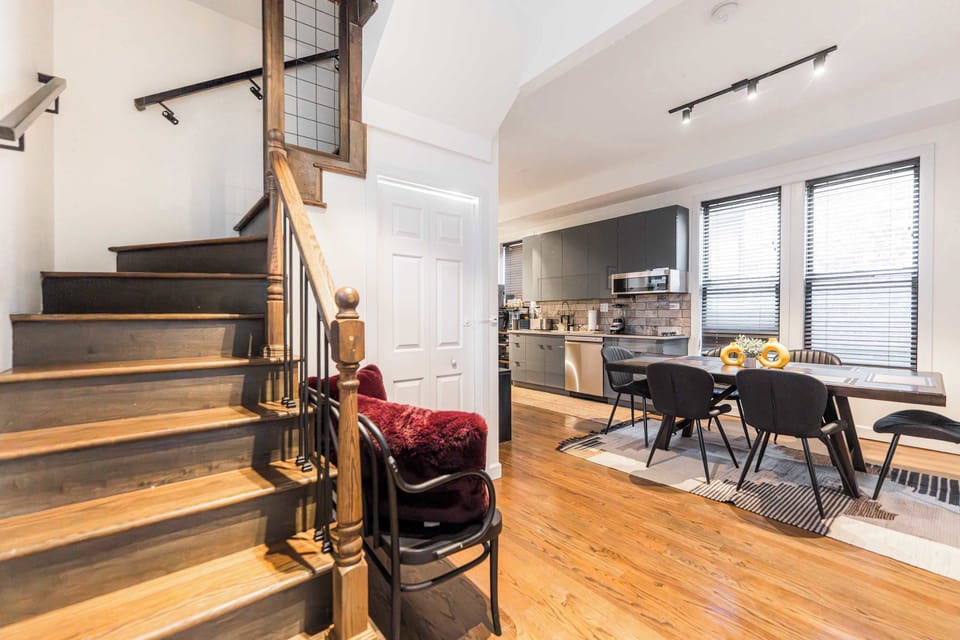 A stylish landing with hardwood floors leads to the upper bedrooms. This cozy nook features a vintage-inspired sideboard, a decorative bench with plush red pillows, and a classic staircase with wrought-iron spindles.