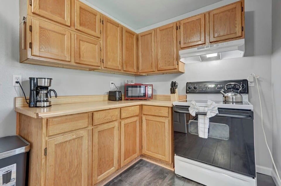 Functional kitchen with warm wood cabinetry, stove, microwave, coffee maker, and toaster, giving you everything in view to cook a simple meal or start the day with a fresh cup of coffee.
