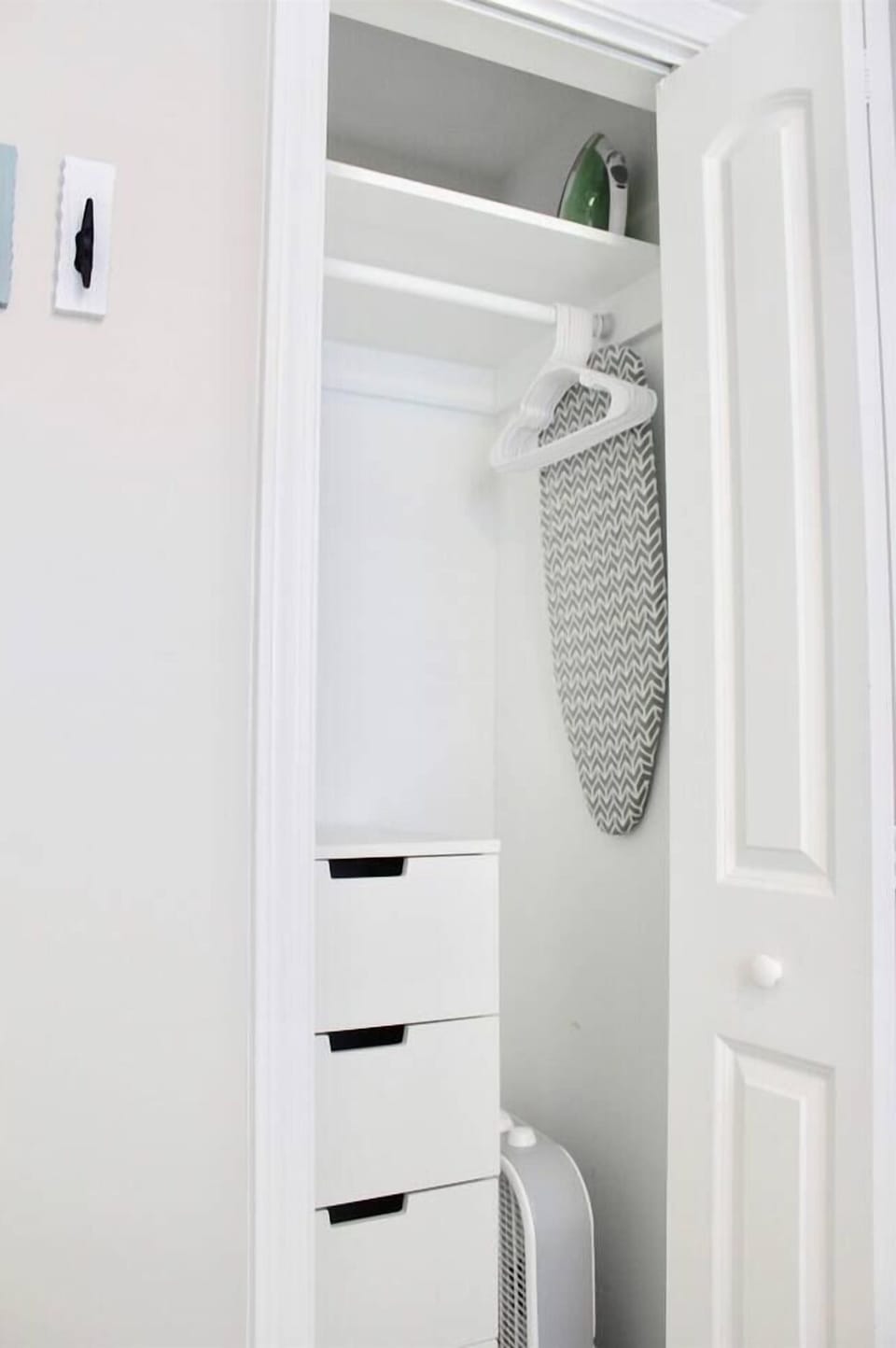 Efficiency dresser, hangers, box fan, iron, and ironing board located in master bedroom closet