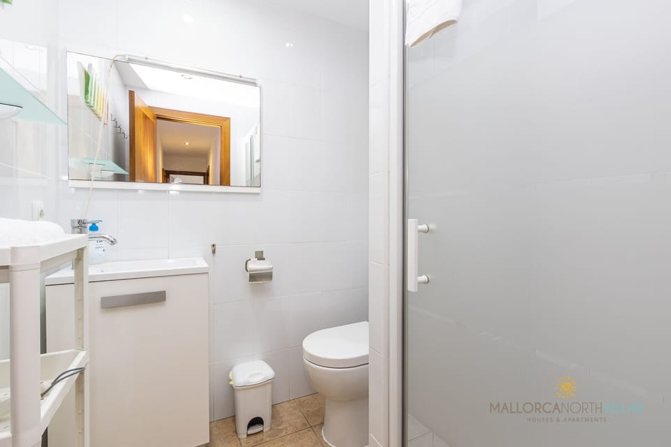 Modern bathroom with frosted glass shower, white sink cabinet and light-colored tiles.