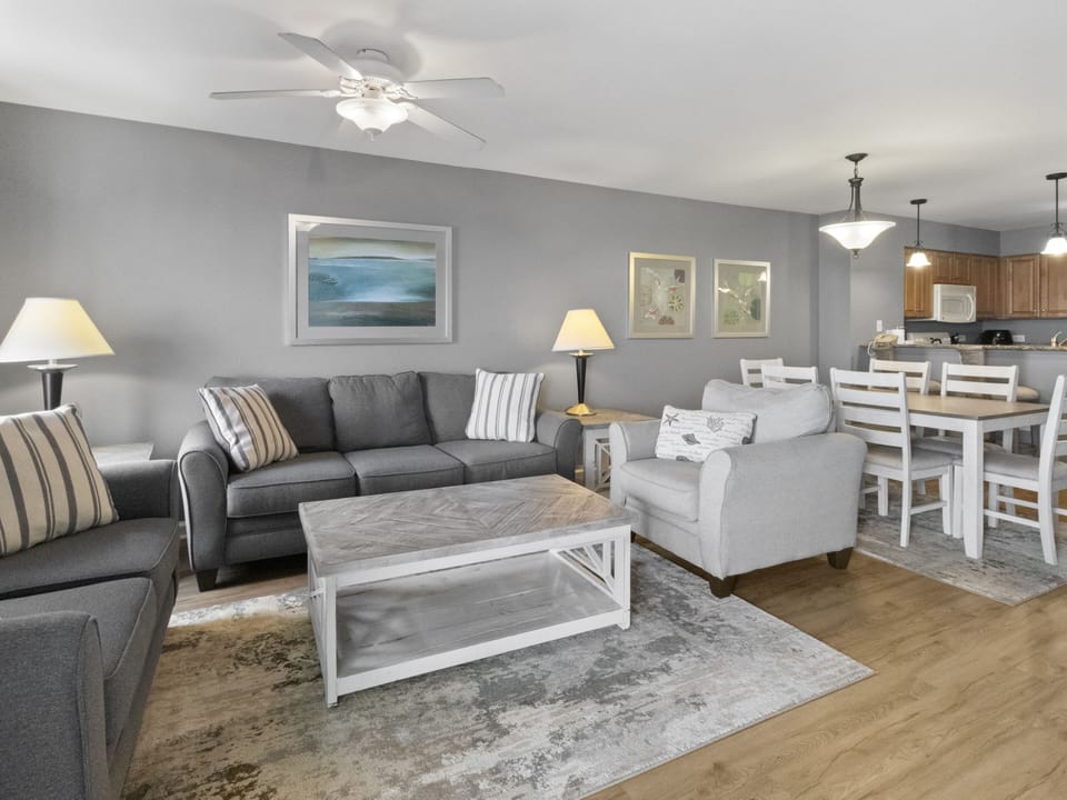 Unwind in your spacious open-concept living area featuring comfortable grey seating, coastal artwork, and modern amenities for perfect relaxation.