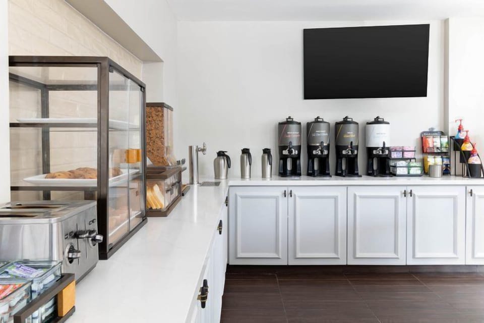 Breakfast station counter with coffee dispensers, thermal carafes, a glass pastry display case, and cereal dispenser