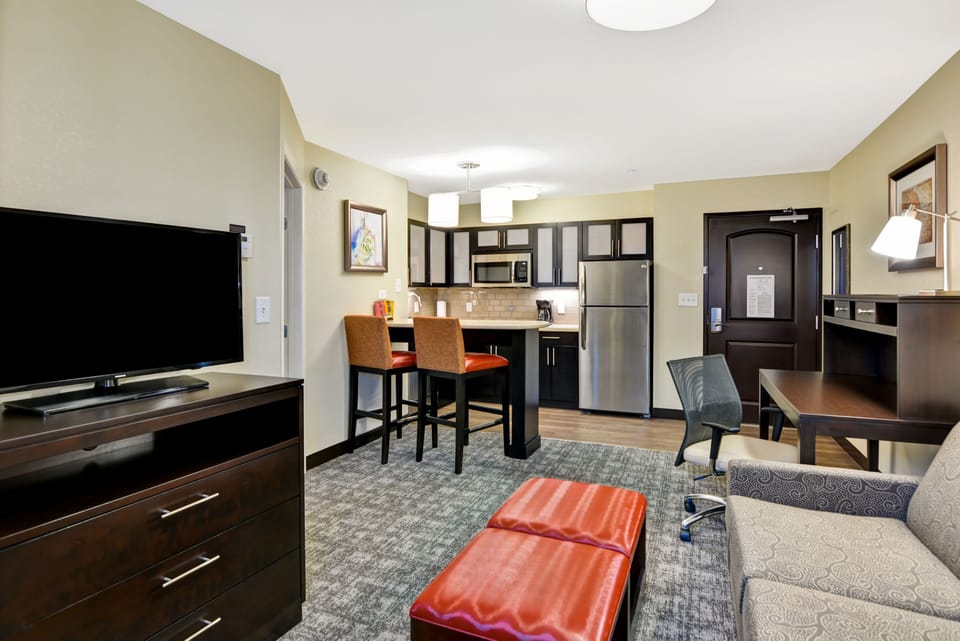 Living area with kitchenette, bar stools, sofa, and TV.