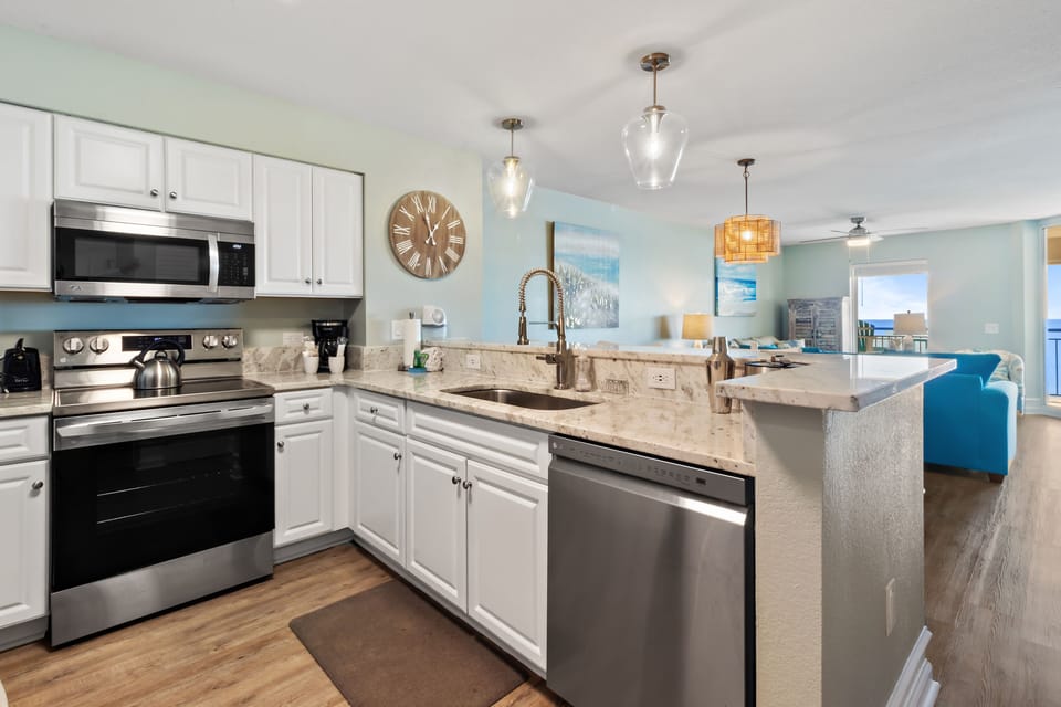 Your fully equipped kitchen awaits with stainless appliances, granite counters, and bright coastal design—perfect for preparing meals.