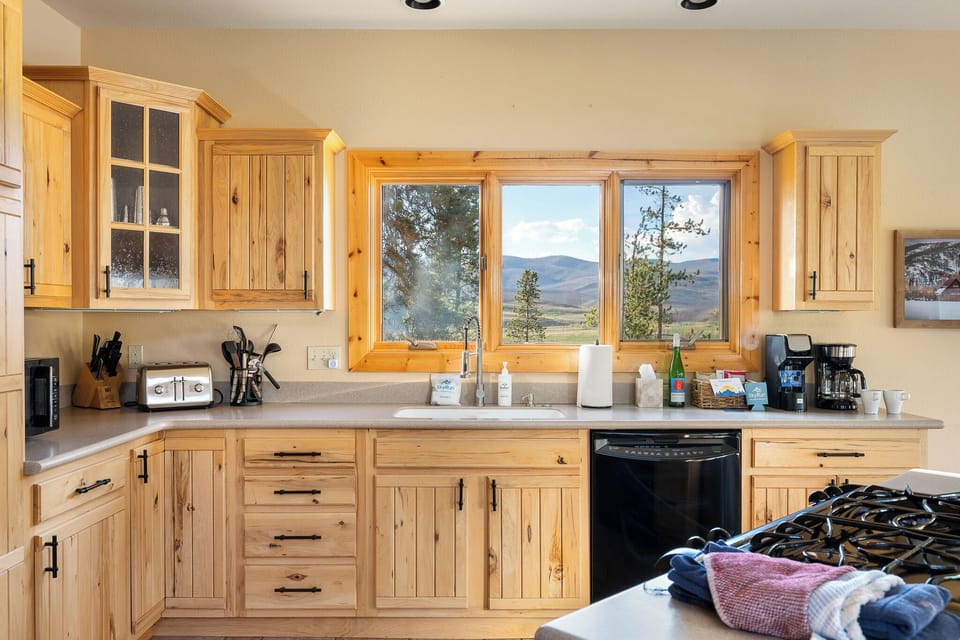 Your fully equipped kitchen features charming wood cabinetry and breathtaking mountain vistas through large windows—perfect for savoring your morning coffee while soaking in the natural beauty.