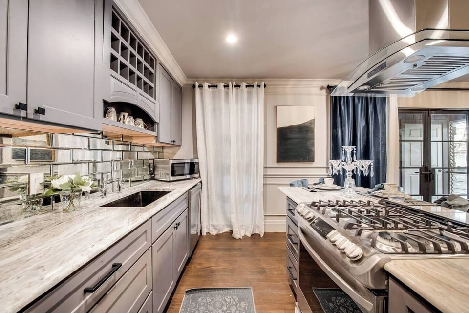 A bright, fully equipped gourmet kitchen with a gas range and stainless steel vent hood, perfect for cooking and entertaining. Opening the French doors elevates the atmosphere, making it an ideal space for special gatherings with friends and family.