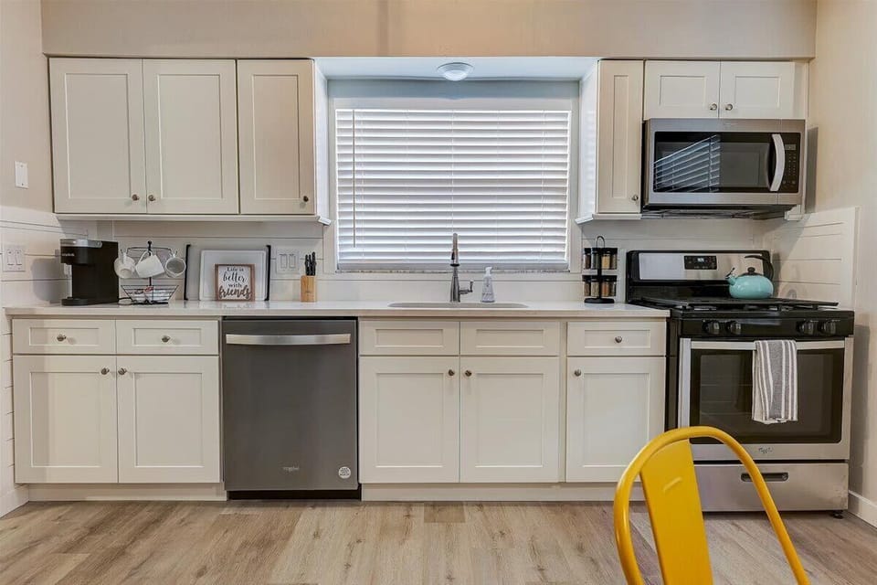Kitchen with Keurig, dishwasher, oven, microwave, kettle, dining area, full sized fridge, spice rack, and kitchen supplies.