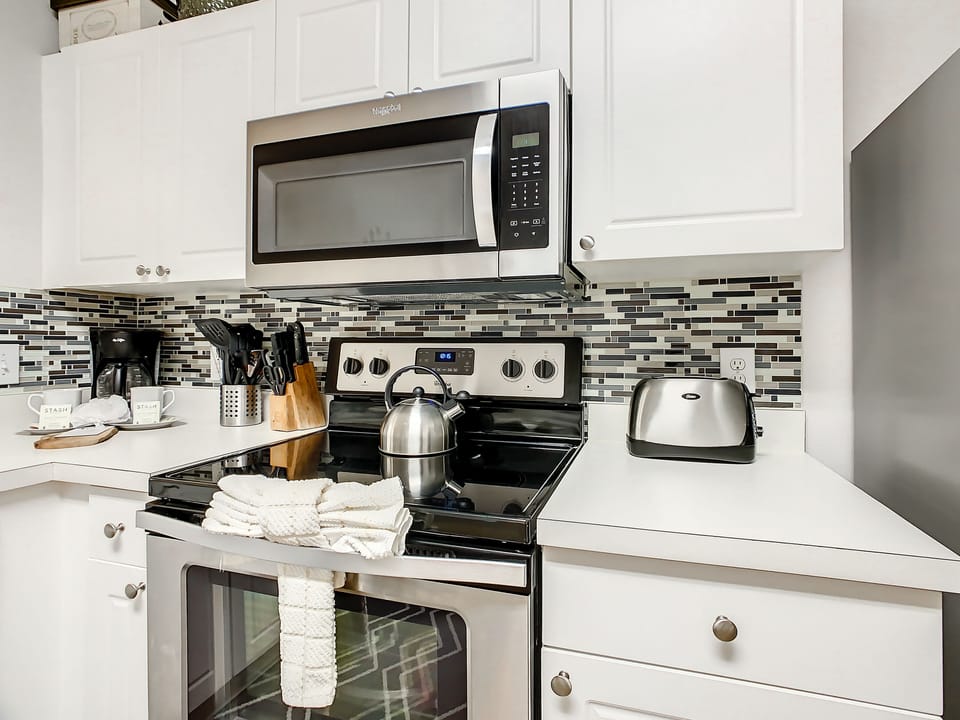 Fully stocked kitchen with stainless steel appliances and sleek backsplash.