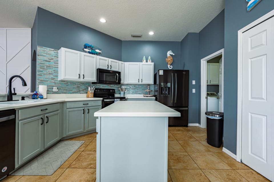 Cook like you mean it — the kitchen has a full island, teal tile backsplash, and black stainless everything