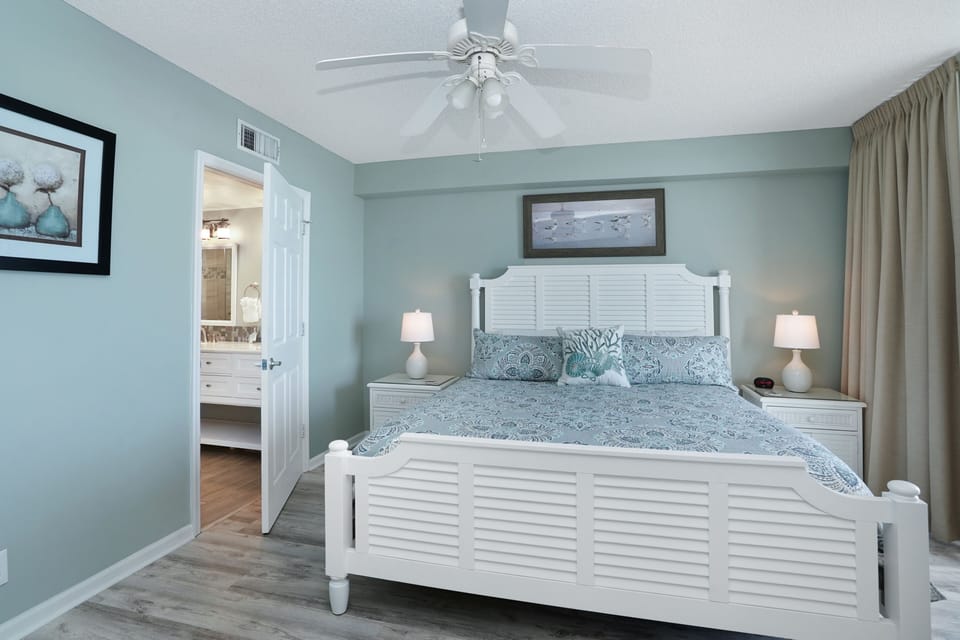 Drift off in your coastal-inspired bedroom with crisp white furnishings, soothing blue tones, and gentle ceiling fan breezes creating the perfect retreat.