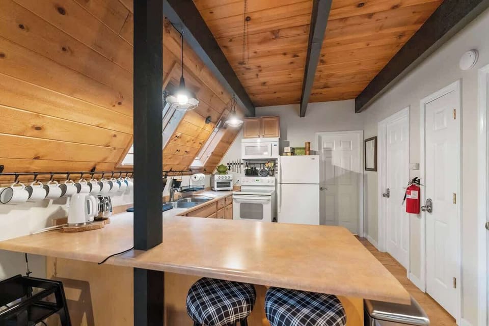Hang out here on the bar stools and visit over coffee or keep the chef company. Access to the bathroom and the downstairs bedroom is located to the right of the refrigerator. There is a visible fire extinguisher for safety.