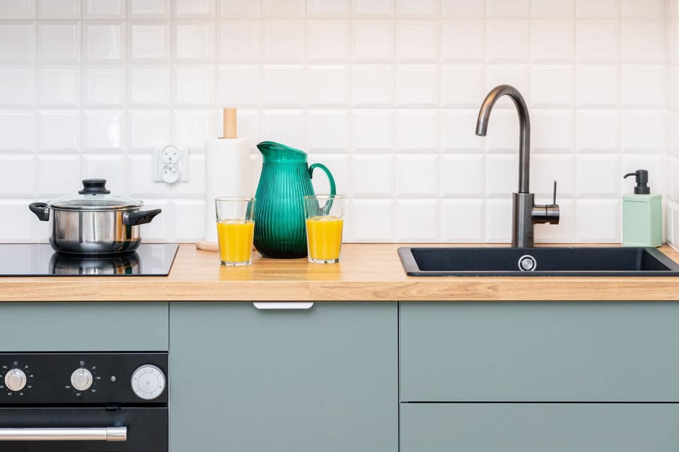A close-up of the kitchen counter with a few items, including a teapot and glasses, against a white-tiled backsplash.