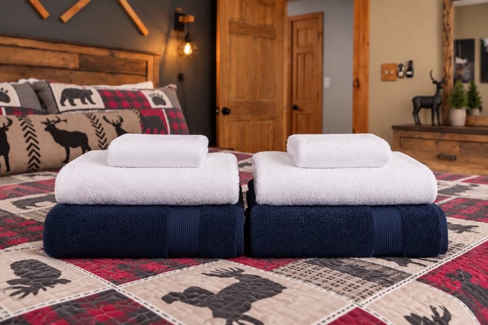 Folded bath towels, hand towels, and washcloths in white and navy, stacked on the primary bed.
