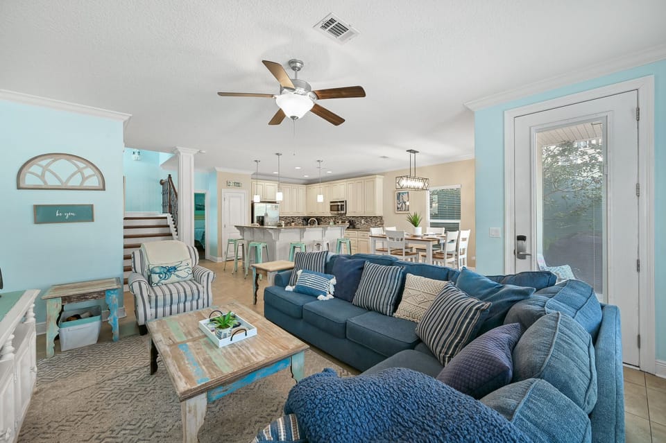 Relax in your spacious living room with plush blue sectional seating, coastal decor, and open kitchen views.