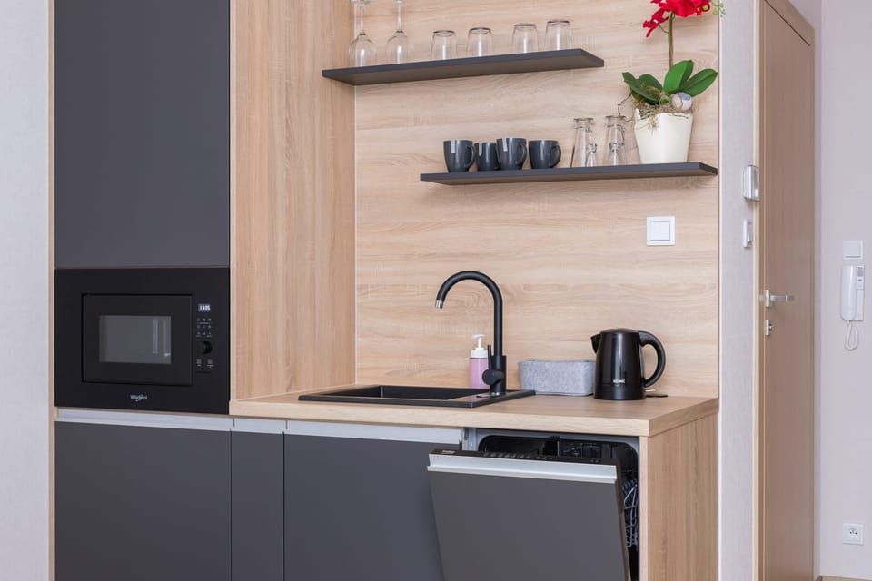 A kitchen area with wooden cabinets, a black countertop, and a built-in microwave and kettle.
