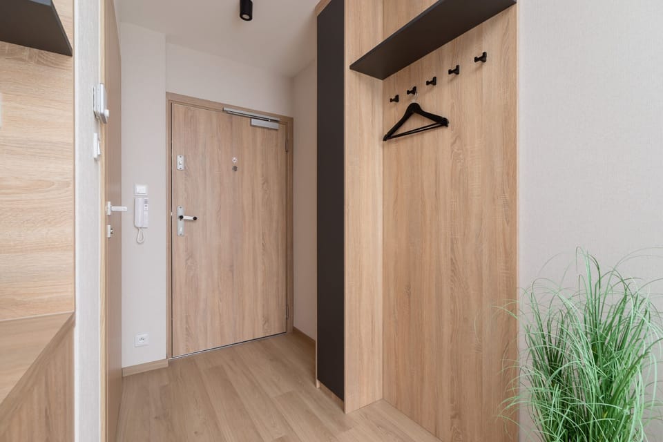 A hallway near the entrance with wooden flooring and a decorative plant in the corner.
