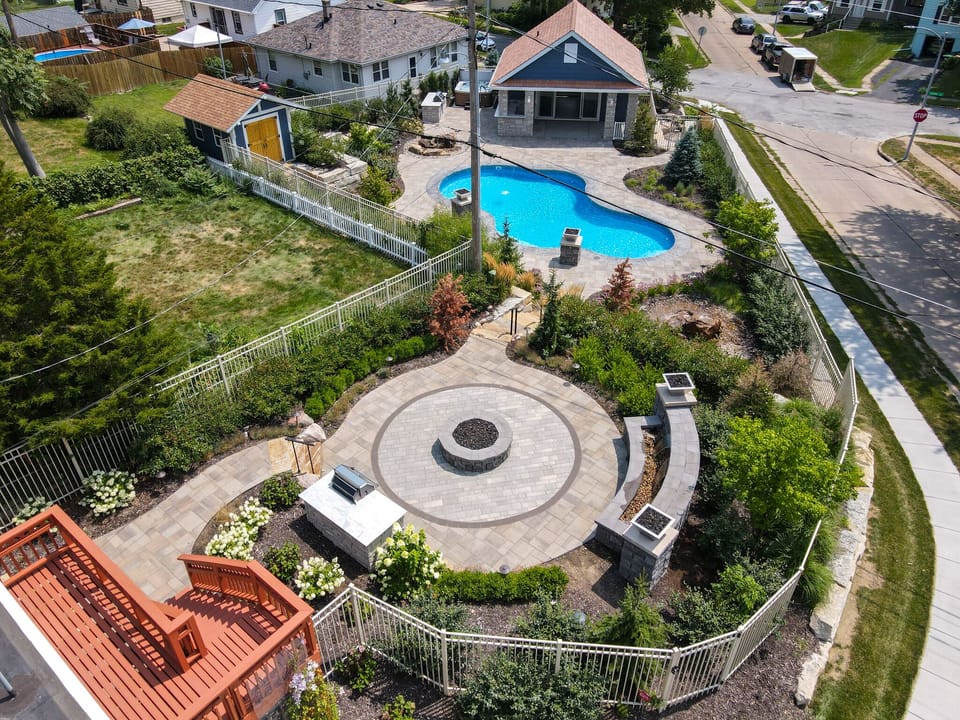 Stunning aerial view of the beautifully landscaped backyard featuring a sparkling swimming pool and fire pit area.