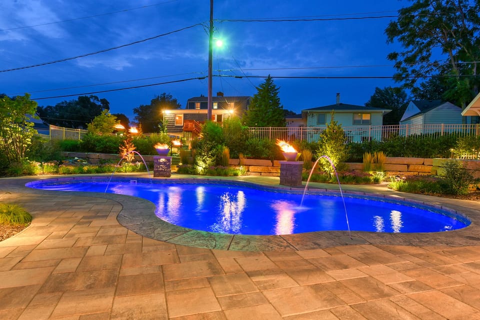 Beautiful illuminated pool area with decorative water features and ambient lighting, surrounded by landscaped gardens in a peaceful residential setting.