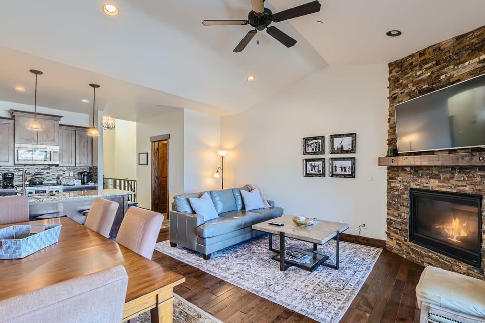 - Living and dining room designed with rustic charm and mountain views  
- Cozy sofa and stone fireplace create the perfect gathering space  
- Open layout connects easily to kitchen for family and friends