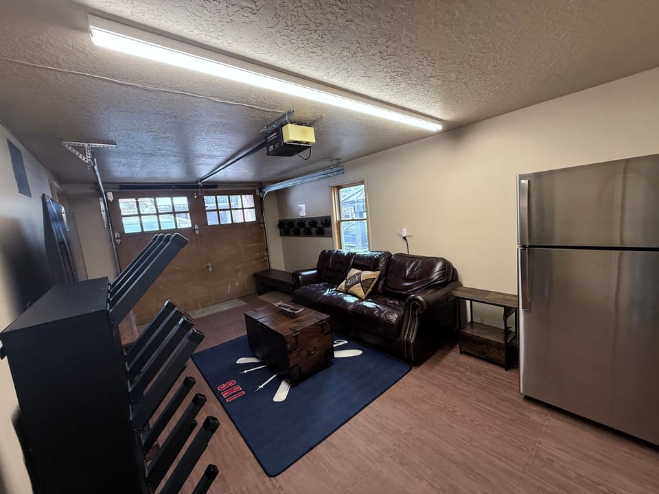 Spacious garage recreation room with lounge seating, storage, and flexible open space. Ideal for casual gatherings, gear organization, or a relaxed hangout area.