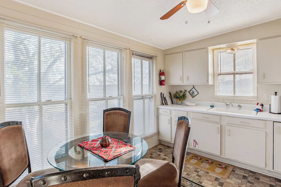 A sun-drenched dining nook features a glass-top table with Southwestern-style chairs, situated next to large windows that offer a bright, airy atmosphere for morning coffee or casual meals.