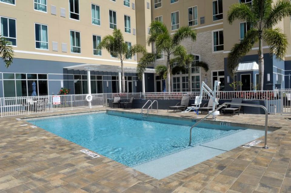 Outdoor pool surrounded by lounge chairs and palm trees.