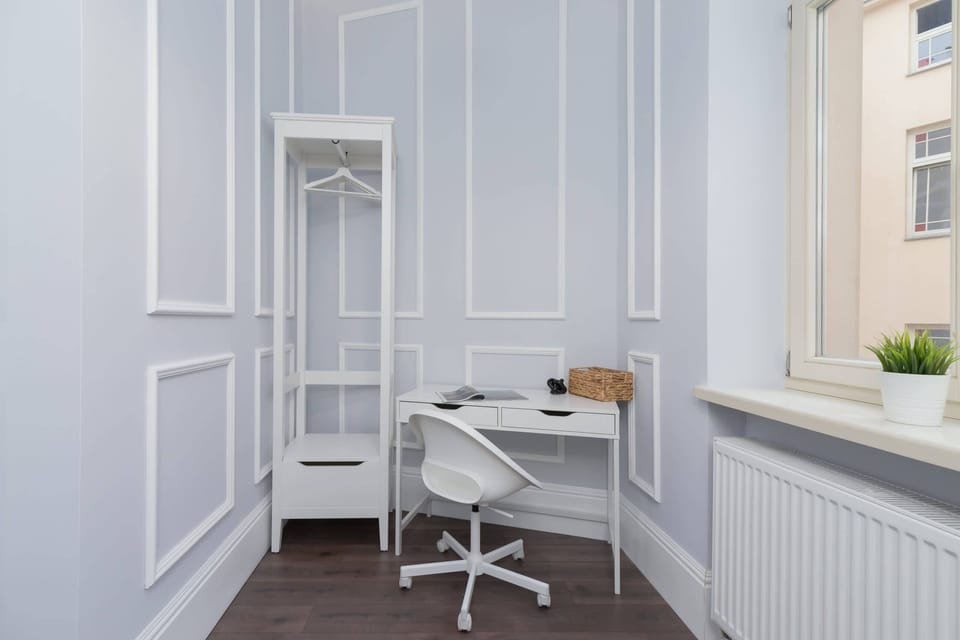 A small workspace with a white desk, chair, and a window letting in natural light.
