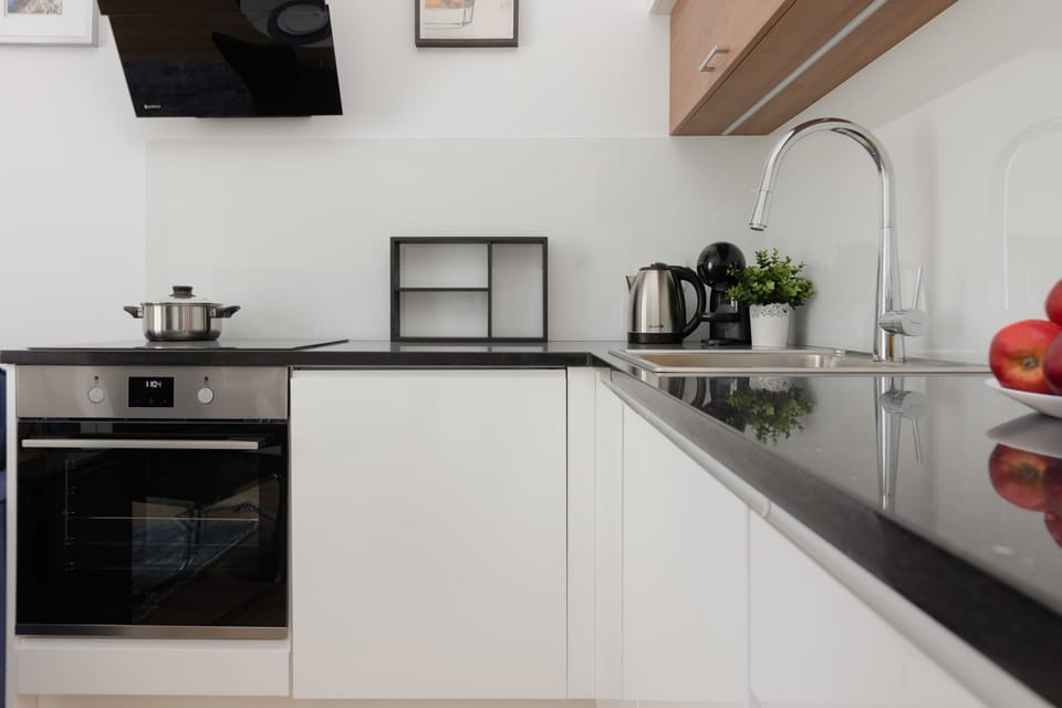 A compact, sleek kitchen with white cabinetry, black countertops, and modern appliances.
