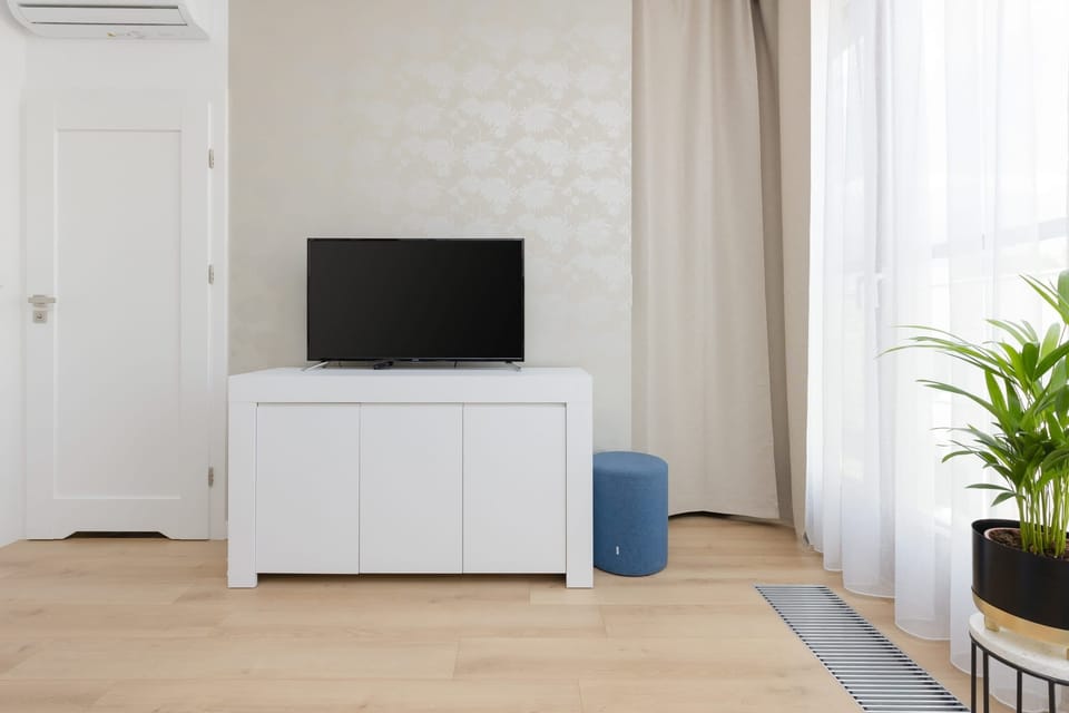A minimalist living room corner with a white TV stand, television, and light curtains complementing the clean design.
